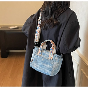 Detail of light blue denim tote with floral embroidery strap and pearl button accent