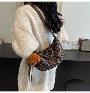 Detail view of leopard print crescent bag with brown leather strap and plush dog charm