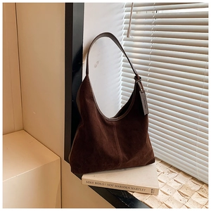 Détail d'un sac hobo en daim marron foncé avec étiquette logo posé sur un rebord