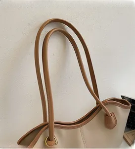 Detail view of large tote bag featuring smooth brown leather straps and beige material