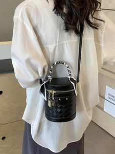 Chic black cylinder bucket bag with woven texture and scarf-wrapped handle shown on model