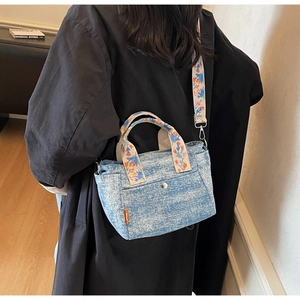 Close-up of vibrant floral embroidery on denim tote bag handles and wide shoulder strap