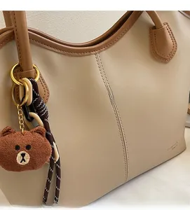 Close-up of beige leather tote bag with brown trim, golden ring hardware and bear charm