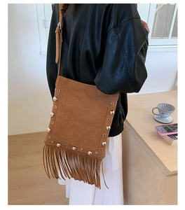 Brown suede crossbody bag with fringe and silver studs shown from a side view on a model