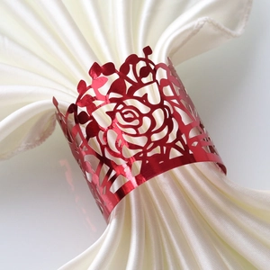 Detail of red hollowed-out rose napkin ring on white satin fabric for wedding table