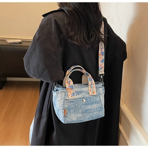 Detail of denim tote bag with floral embroidery strap worn by a model in black trench coat