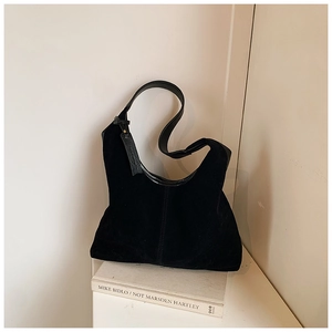Détail du sac hobo en daim noir mat sur un livre blanc avec bandoulière en cuir