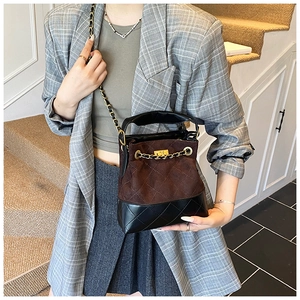 Detail of a brown suede bucket bag with black leather patchwork and gold chain strap