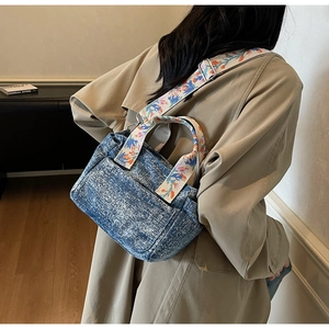Detailed back view of a blue washed denim crossbody bag with a floral embroidered strap