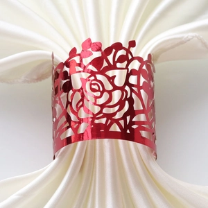 Detailed laser-cut red rose napkin ring with intricate petals on white satin cloth