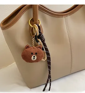 Detail of cartoon bear plush charm with gold keyring on a khaki tote bag accessory
