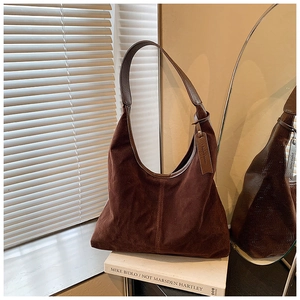 Vue détaillée du sac hobo en daim marron foncé avec bandoulière sur livre d'art