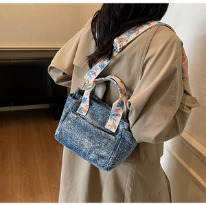Close-up of blue denim crossbody bag featuring an embroidered floral shoulder strap