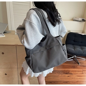 Dettaglio di una borsa tote in tela grigio scuro con tasca laterale indossata da una modella