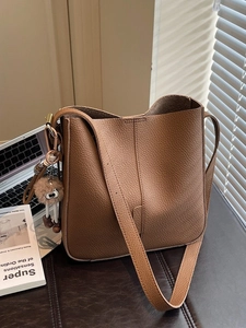 Brown lychee leather bucket bag with plush charm on a textured leather background