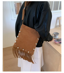 Detail of brown suede crossbody bag featuring retro bohemian tassels and silver rivets