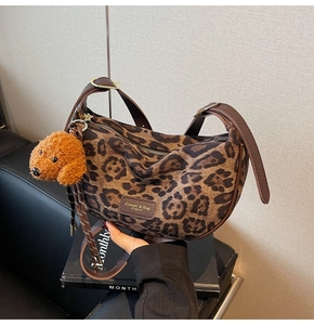 Close-up of leopard print canvas bag with brown leather strap and plush dog charm