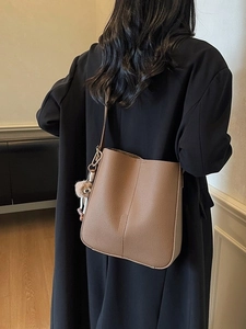 Vintage brown leather bucket bag for women with pompom detail worn with a black wool coat