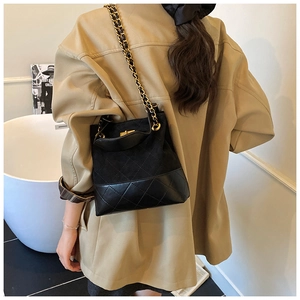 Detail of a quilted contrast bucket bag with gold chain strap on a model shoulder
