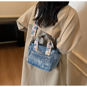 Detail of blue denim tote bag with colorful floral embroidered handle and wide strap