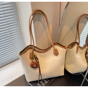 Detail of cream tote bag with brown trim featuring a plush bear charm on its handle