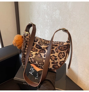 Detail view of leopard print shoulder bag with plush bear charm and leather strap