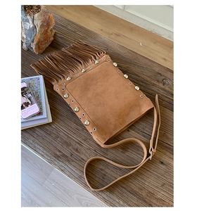 Detail of brown suede crossbody bag featuring bohemian fringe and silver metal rivets