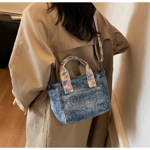Detail of denim crossbody bag with colorful floral embroidered wide strap and worn-out texture