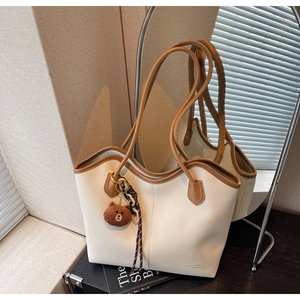 Detail view of stylish beige tote bag with brown leather handles and woven lanyard