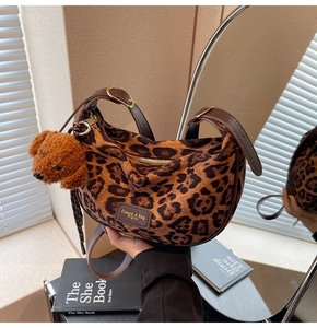 Detail of leopard print crescent bag featuring a plush dog charm and adjustable leather strap