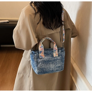 Detail of blue denim tote bag with vintage wash and colorful floral embroidery strap