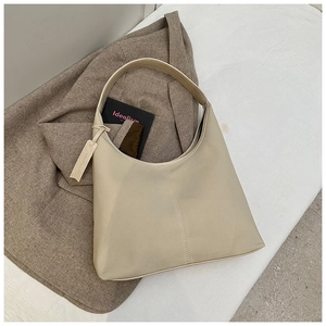 Vue détaillée du sac seau beige minimaliste posé sur une veste de blazer marron