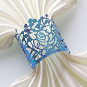 Macro detail of iridescent laser-cut rose napkin ring on elegant white satin napkin