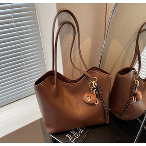 Detail of a dark brown matte leather tote bag with a cute bear plush charm and woven rope