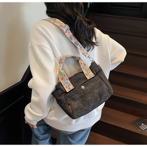 Detail of grey canvas tote featuring colorful floral embroidered strap and metal snap button