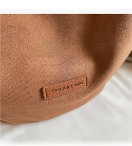Detail showing soft brown suede texture and leather brand patch on the tote bag