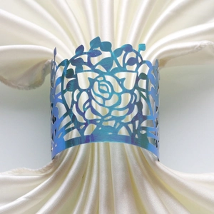 Detail view of laser-cut iridescent blue rose napkin ring on white satin fabric