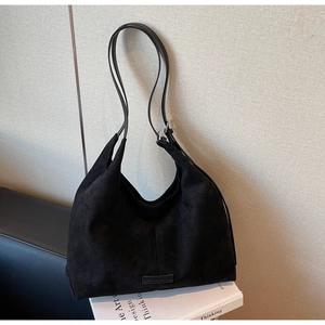 Dettaglio di borsa tote in pelle scamosciata nera con logo e cuciture rifinite a mano