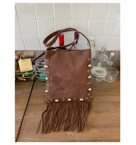 Close-up of brown suede crossbody bag with vintage rivets and bohemian long fringe details