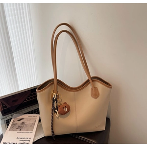 Detail of beige leather tote bag with vertical stitching and brown bear plush charm