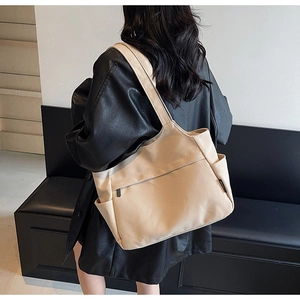 Vista dettagliata della borsa tote in tela beige con tasche laterali sulla spalla del modello
