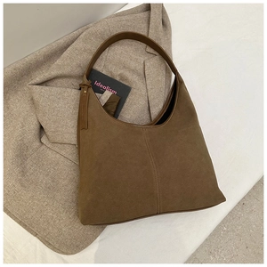 Détail d'un sac hobo en daim marron avec large bandoulière et pendentif minimaliste