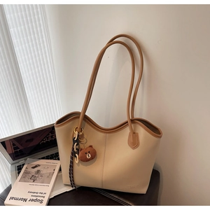 Detail of beige tote bag with brown trim and plush bear charm on a leather seat