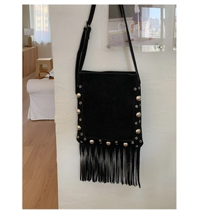 Detail of black suede shoulder bag with silver studs and long tassels on white wall