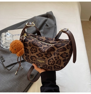 Detail view of leopard print shoulder bag with plush dog charm on white bedding background
