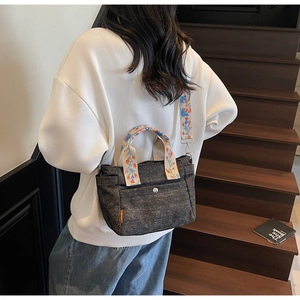 Detail of dark grey denim tote with colorful floral embroidery on the shoulder strap