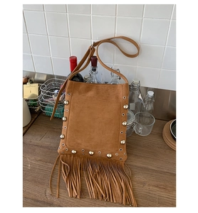 Detail of brown suede shoulder bag featuring silver rivets and long fringe tassels