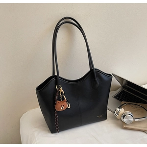 Close-up of black leather tote bag with fine stitching and a cute bear accessory