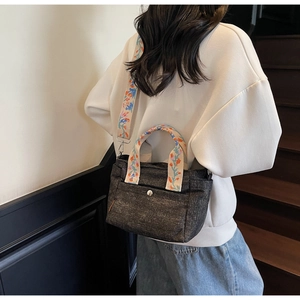 Detail of denim tote bag with colorful floral embroidery on straps and wide shoulder belt