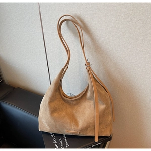 Dettaglio borsa hobo in camoscio marrone con tracolla regolabile su un divano